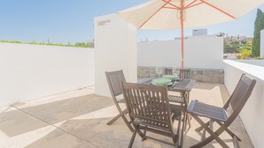 An outdoor patio with a table and chairs, a beige umbrella, and a view of the cityscape. - Melro's Places (Setúbal)