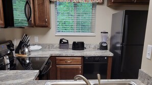 Una cocina con encimeras de granito, un lavamanos de acero inoxidable, un refrigerador negro y armarios de madera.