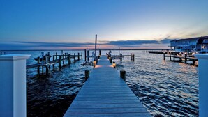 Un muelle de madera se extiende sobre aguas tranquilas al atardecer, con un edificio a la derecha.