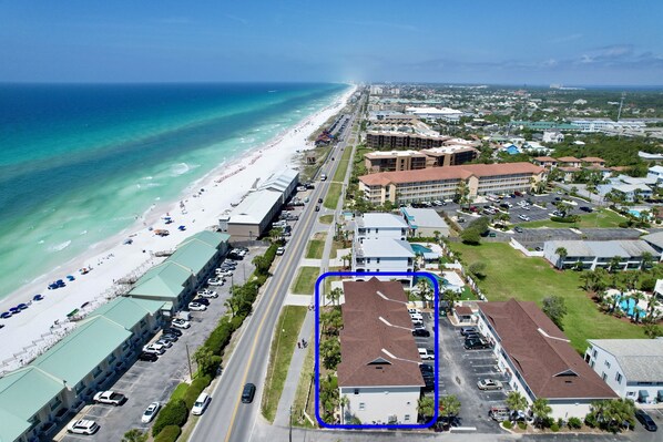 An aerial view of a coastal hotel with a parking lot, beach access, and a view of the ocean.