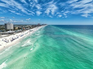 A coastal beach with clear turquoise waters, a sandy shore, and buildings along the coastline. - Fall Specials! 4bed4bath, 2nd row, Private beach, Tiki room! (Miramar Beach)