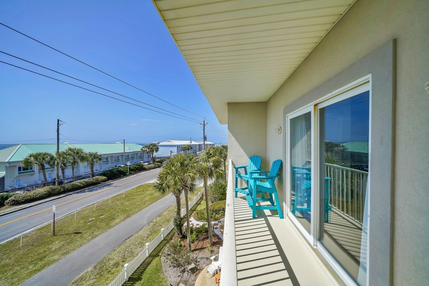 Un balcon avec des chaises turquoise, une vue sur la route et, au loin, un bâtiment doté d’un toit végétalisé.