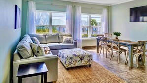 Een woonkamer met een bank, voetenbankje, eettafel, stoelen en een plafondventilator.