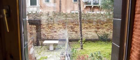 A courtyard with a stone bench, potted plants, and a brick wall.