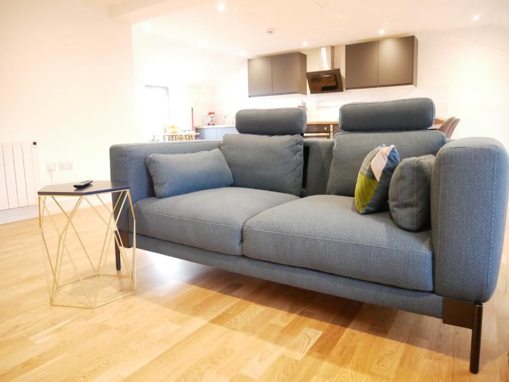 A modern living room with a grey sofa, a small side table, and a kitchen in the background.