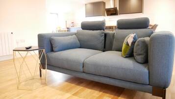 A modern living room with a grey sofa, a small side table, and a kitchen in the background.