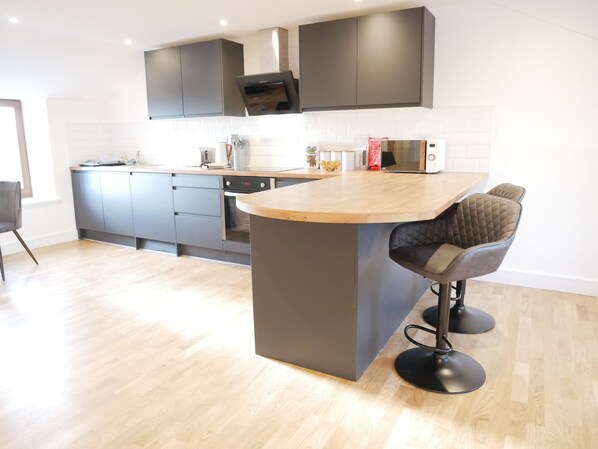A modern kitchen with grey cabinets, a wooden countertop, and a built-in oven. - Scandic House (Ulverston)