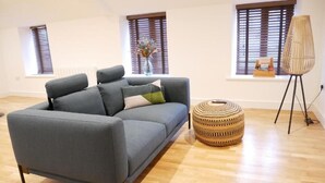 Un salon moderne avec un canapé gris, un pouf en osier et un grand lampadaire.