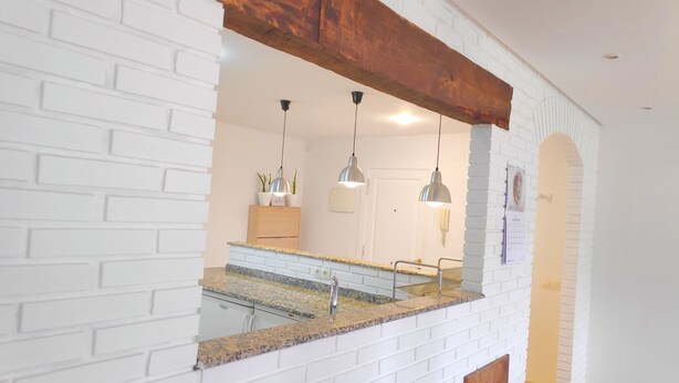 A modern kitchen with white brick walls, granite countertops, and pendant lighting.