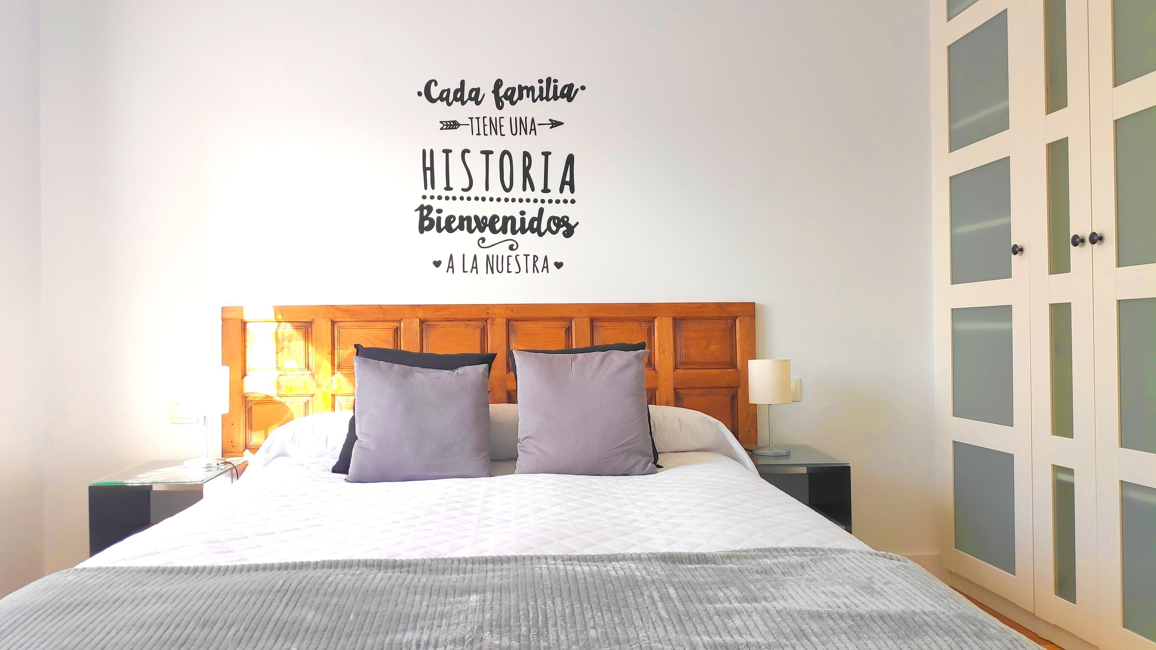 Een hotelkamer met een bed, twee kussens, een nachtkastje met een lamp en een inloopkast met ruitverdelingen.
