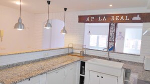 A kitchen with granite countertops, white cabinets, pendant lights, a window with a view, and a sign that reads "AP LA REAL".