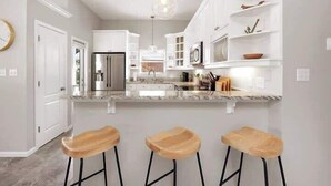 Una cocina moderna con armarios blancos, un refrigerador de acero inoxidable, una encimera de mármol y tres taburetes de madera.