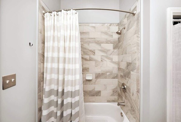 Un espace douche doté d’une pomme de douche incurvée, d’un porte-serviettes et d’un savonnetteur.
