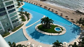 Ett semesterhotell med en stor pool, en strand och en modern byggnad.