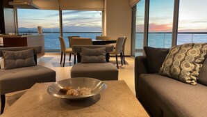 Ett modernt vardagsrum med ett stort fönster med utsikt över havet, en matplats och en sittgrupp med en dekorativ skål på ett bord.