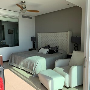 A modern bedroom with a large bed, a ceiling fan, a nightstand, a lamp, and a view of the outside. - Condominio Frente a Playa Peninsula Puerto Vallarta Jalisco (Puerto Vallarta)