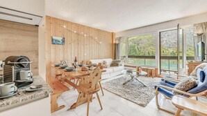 Un salon moderne avec un coin repas en bois, un canapé et une vue sur un paysage montagneux grâce à de grandes fenêtres.