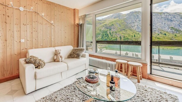 Un salon moderne avec un canapé blanc, une table basse en verre et une vue sur les montagnes, visible à travers de grandes fenêtres.