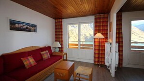 A cozy room with a red sofa, wooden table, and curtains. - 100m from ski slopes, 4th floor, view lake/mountain, balcony, tv, ski locker, 62m², Tignes (Tignes)