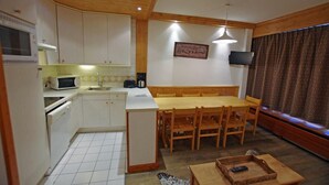 A compact kitchen with white cabinets, a microwave, and a coffee maker. There is a wooden dining table with chairs and a TV mounted on the wall.