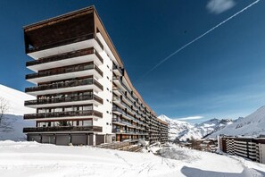 A multi-story hotel with balconies, set against a snowy mountain backdrop.