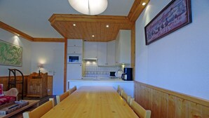 A dining area with a wooden table and chairs, a kitchen with white cabinets, and a framed picture on the wall.