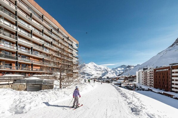 A ski resort with a snow-covered path, a person skiing, and buildings with balconies.
