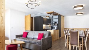 A modern living room with a grey sofa, red cushions, a wooden dining table, and a kitchen area in the background. - Wifi, 100m from ski slopes, fitness, swimming pool, sauna, jacuzzi, hammam, balcony (Val Thorens)