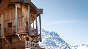 A wooden chalet with multiple balconies, set against a backdrop of snow-covered mountains. - Wifi, 100m from ski slopes, fitness, swimming pool, sauna, jacuzzi, hammam, balcony (Val Thorens)