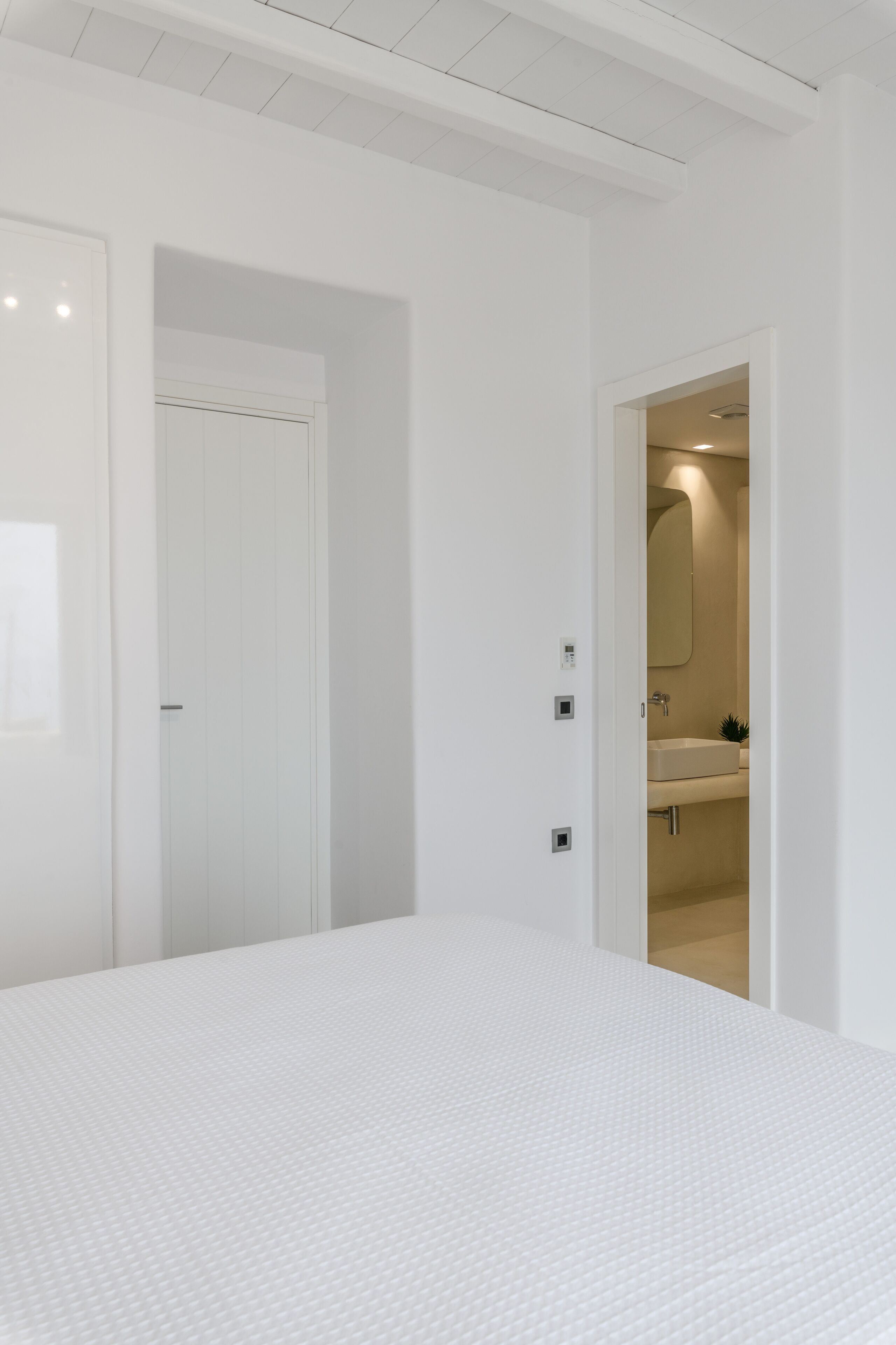 A bedroom with a large bed, a white door, and a bathroom visible through an open door.