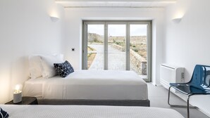 Ein modernes Schlafzimmer mit einem großen Bett, einem Sessel und Blick auf einen steinbelagten Weg.