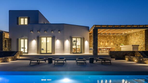 Ein modernes Haus mit Pool, Sitzgelegenheit im Freien und einer Steinmauer.