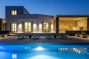 Una casa moderna con piscina, zona de estar exterior y un muro de piedra.