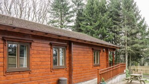 A wooden cabin with a porch, windows, and a small trash can. - Chloe's Lodge (Pickering)