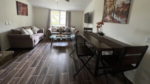 A living room with a sofa, a coffee table, a dining table with chairs, a ceiling fan, a TV mounted on the wall, and a window with curtains. - Newly renovated centrally located apartment in La Crucecita Huatulco Oaxaca  (La Crucecita)