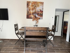 Ein Essbereich mit Holztisch und Stühlen, einem Bild von einem Baumweg und einer Zimmerpflanze.
