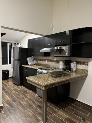 A modern kitchen with dark cabinets, a granite countertop, a stainless steel refrigerator, a stove, and a microwave.