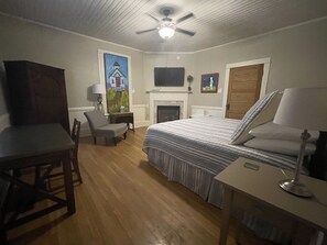 A bedroom with a bed, a desk, a chair, a television, and a fireplace.
