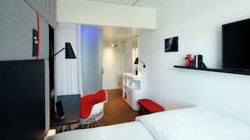 Une chambre d’hôtel moderne équipée d’un lit, d’un bureau avec une chaise, d’une coiffeuse et d’un téléviseur fixé au mur.