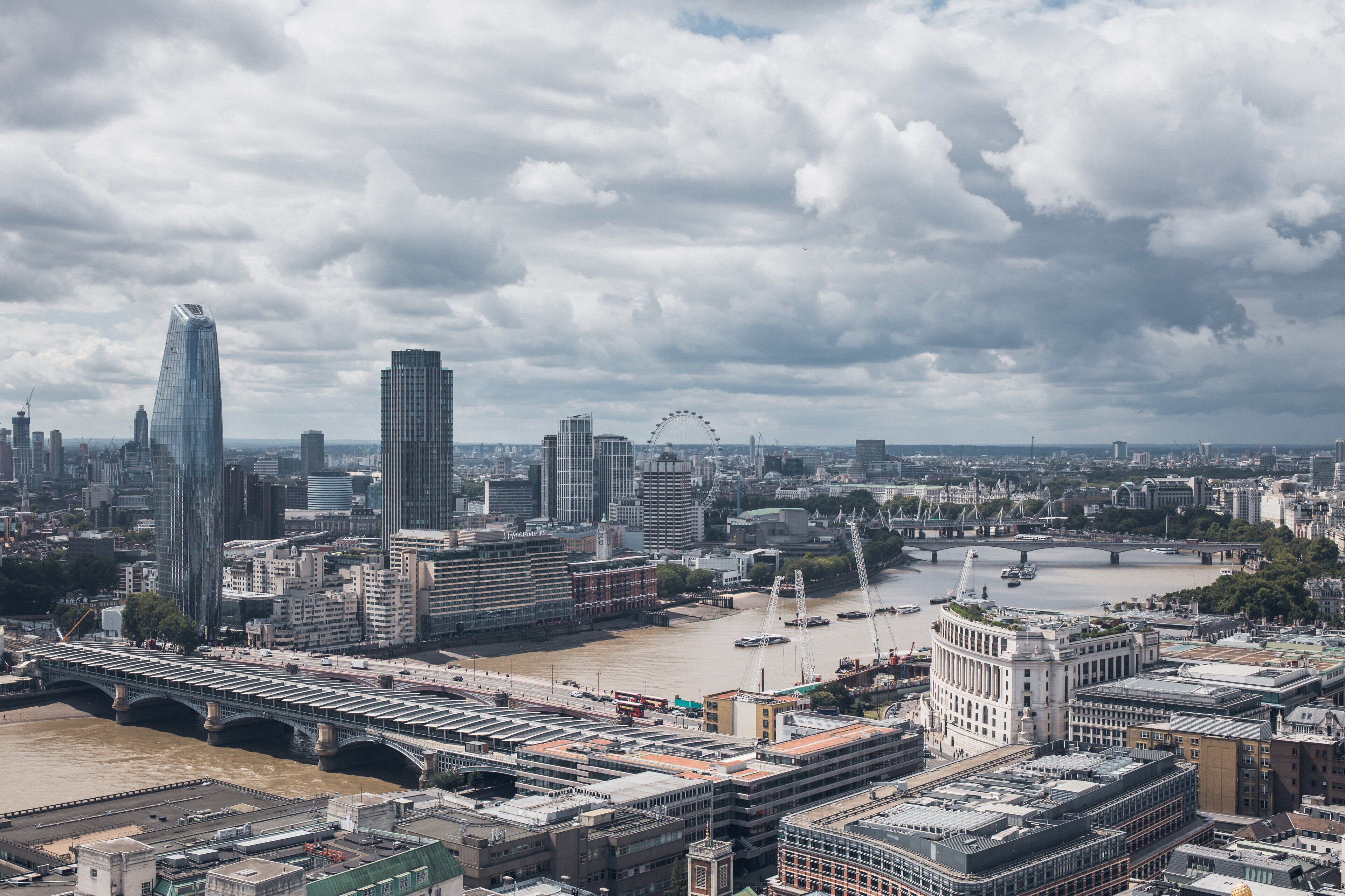 A cityscape with a prominent bridge, a river, and a large Ferris wheel in the distance.