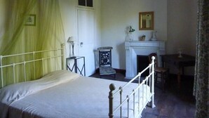 Una habitación con cama, una mesita, una silla, chimenea y ventana.