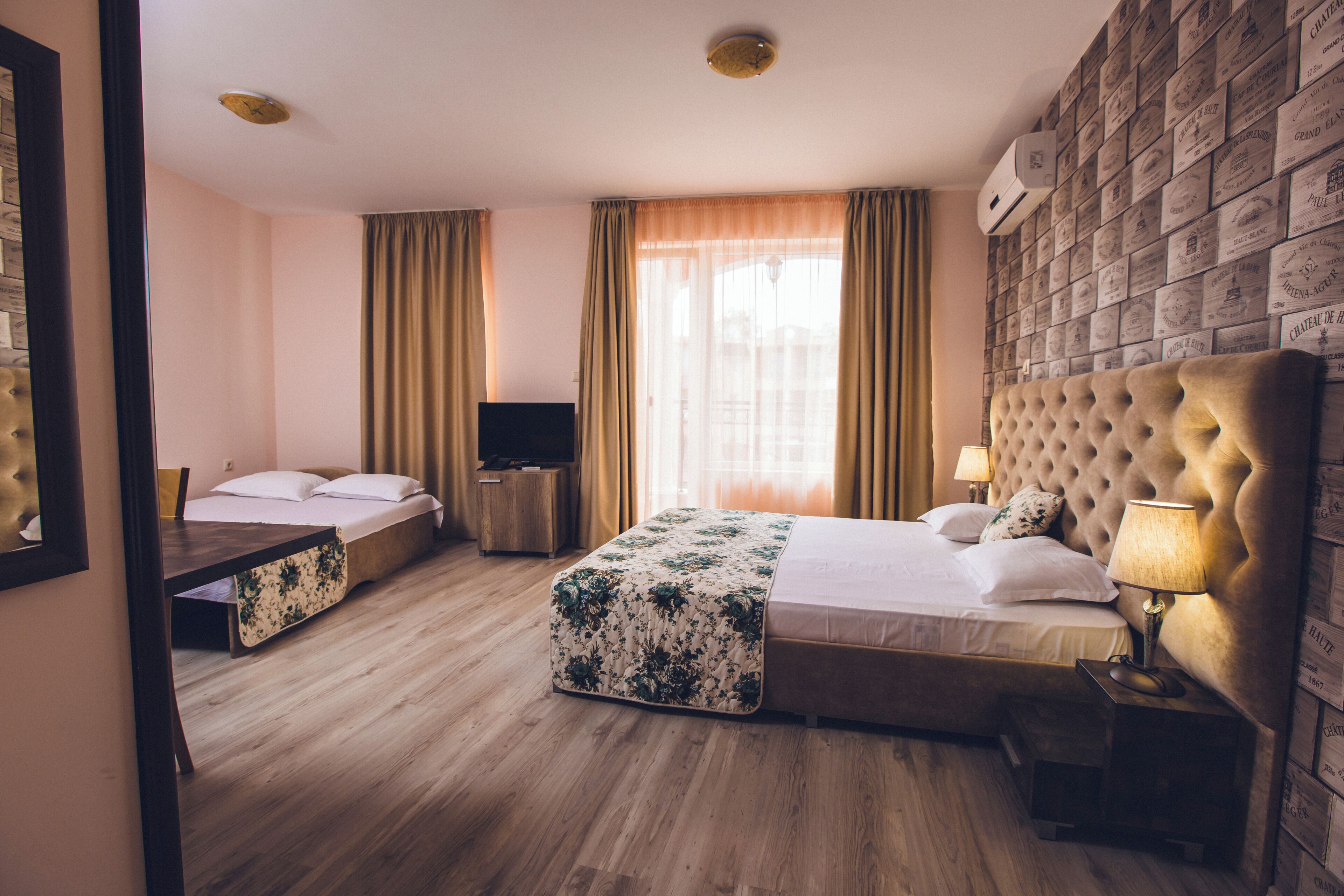 A hotel room with a large bed, a smaller bed, a desk, a TV, and a wall of vintage-style boxes.