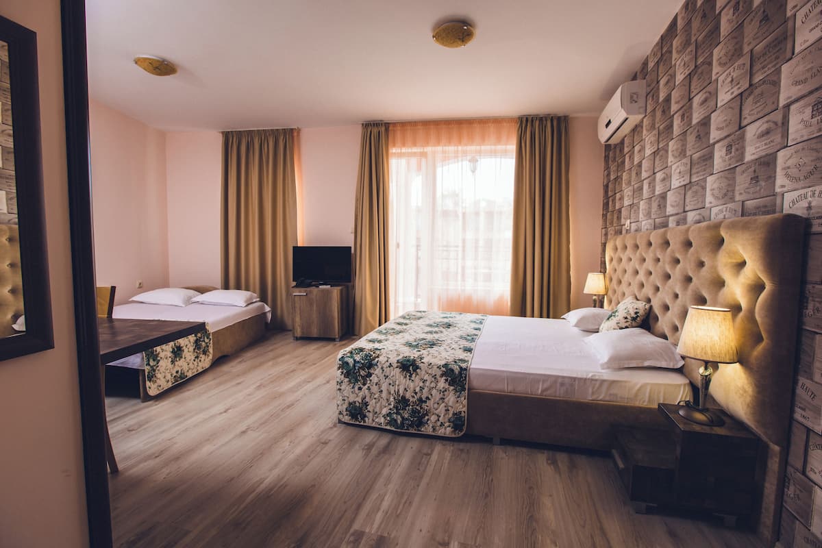 A hotel room with a large bed, a smaller bed, a desk, a TV, and a wall of vintage-style boxes.
