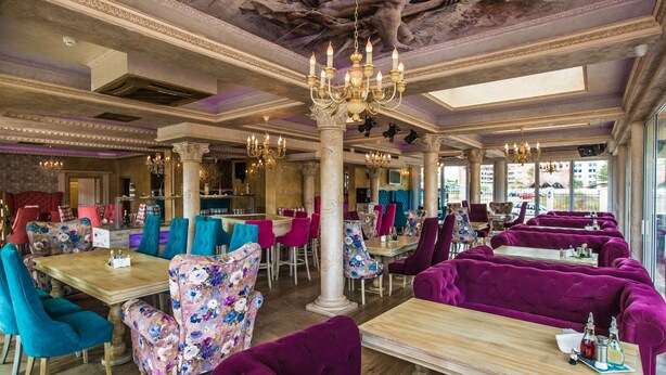 A restaurant with purple and teal upholstered seating, chandeliers, and a classic architectural ceiling. - Avenue Deluxe (Sunny Beach)