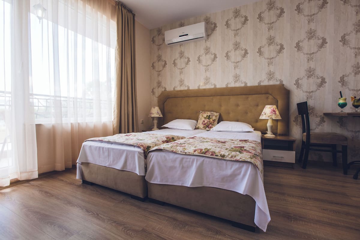 A double bed with floral bedding, a nightstand with lamps, a chair, and a balcony view.