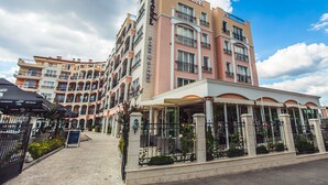 A multi-story hotel with a covered outdoor seating area and a pool. - Avenue Deluxe (Sunny Beach)