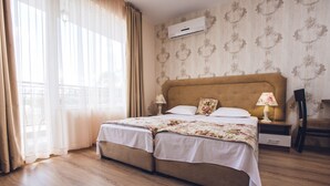 A double bed with floral bedding, a bedside table with a lamp, and a window with curtains. - Avenue Deluxe (Sunny Beach)