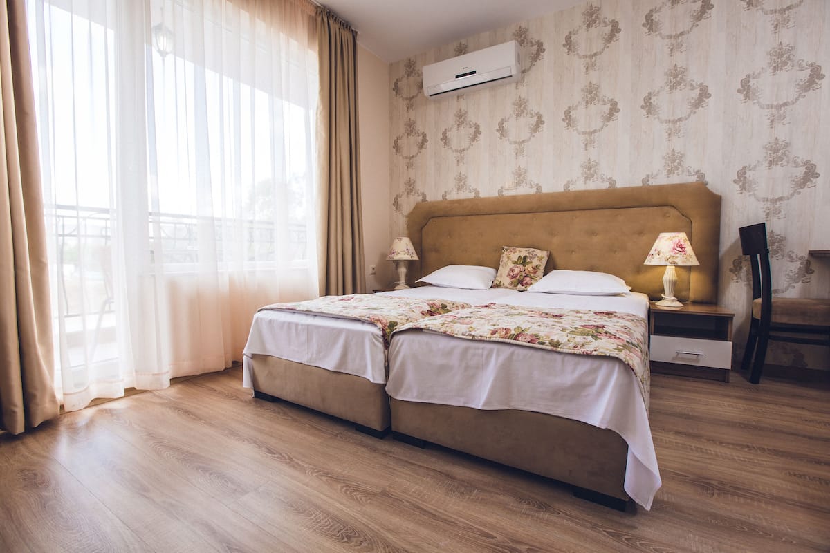 A double bed with floral bedding, a bedside table with a lamp, and a window with curtains.