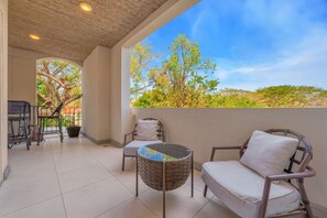 A balcony with two wicker chairs, a small round table, and a view of trees and landscape.