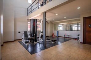 Een ruime fitnessruimte met diverse apparaten, een tussenverdieping en grote ramen voor natuurlijk licht.